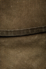 Close-up texture of a canvas fabric backpack. Leather straps and metal buckles. Vintage khaki back.