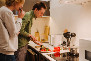 Young gay couple laughing while cooking together in kitchen