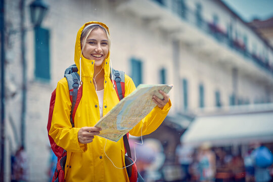 Smiling  woman with a yellow raincoat and map on the street while enjoying a walk through the city on a rainy day.