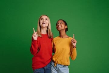 Multiracial girls laughing and hugging while pointing fingers upward