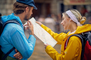 Man and woman  in raincoat with map walks through the old city streets on rainy day