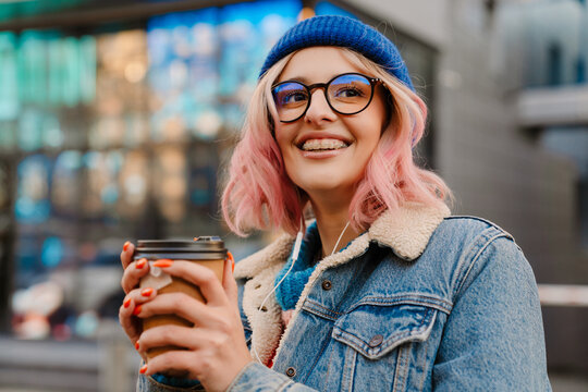 Young woman listening music while drinking coffee on city street