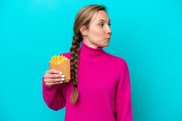 Young caucasian woman holding fried chips isolated on blue background looking to the side