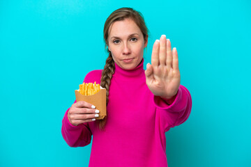 Young caucasian woman holding fried chips isolated on blue background making stop gesture