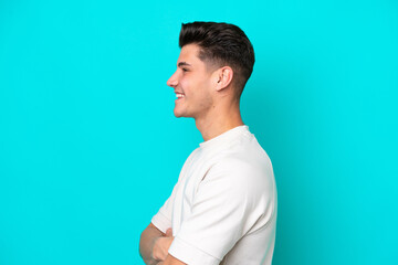 Young handsome caucasian man isolated on blue bakcground in lateral position