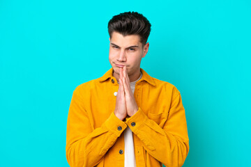 Fototapeta premium Young handsome caucasian man isolated on blue bakcground keeps palm together. Person asks for something