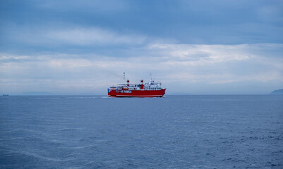 Red ferry boat on rippled sea, blue cloudy sky. Transportation in Meditteranean Sea