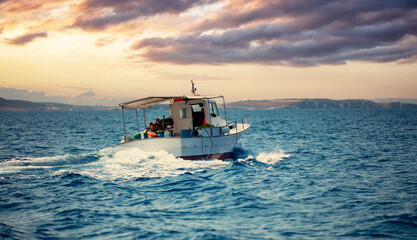 Fishing boat sails in Aegean wavy sea, blue sky at sunset background. Cyclades Greece. - obrazy, fototapety, plakaty