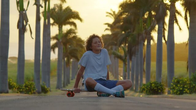 A teenager is skating along a beautiful road with palm trees. Silhouette of a boy with a skateboard