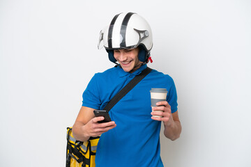 Young caucasian man with thermal backpack isolated on white background holding coffee to take away and a mobile