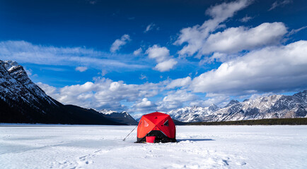 An ice fishing tent for trout fishing standing tall on a frozen lake in the Canadian Rocky...