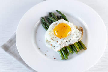 Cooking asparagus. Fried asparagus sprouts and fried eggs on a white plate. Healthy food and diet.
