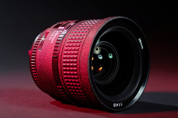 Detailed camera lens with red highlights on a dark paper background.Light reflections in glass lenses.