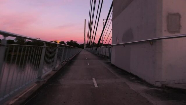 A bicycle ride over a cable-stayed suspension bridge during sun rise where the sky is a beautiful pink colour