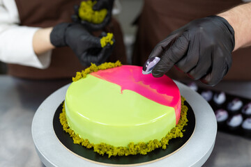 Two confectioners, a man and a woman, decorate a mousse cake with a mirror glaze with handmade...