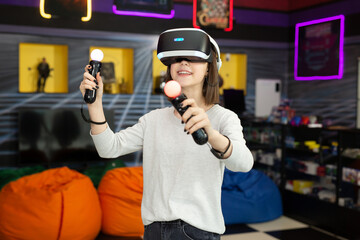 Child, a teenage girl playing on a game console in virtual reality glasses shooting a game with a remote control gun in a game club. VR