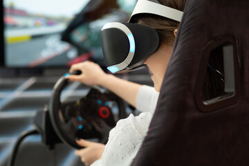Close-up of the hands of a teenage girl in virtual reality glasses, who is holding the steering wheel and playing a computer game on the console.