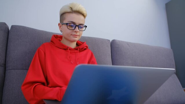Nerd working on computer at home. Portait of young woman with short hair wearing nerdy glass typing text on laptop