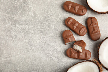 Delicious milk chocolate candy bars with coconut filling on grey table, flat lay. Space for text