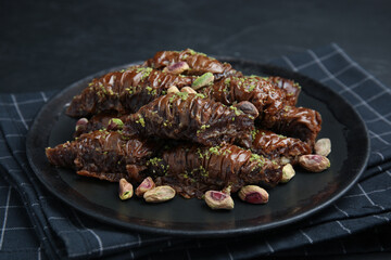 Delicious baklava with pistachio nuts and napkin on black table, closeup