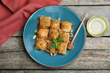 Delicious baklava with pistachios, honey and mint on wooden table, flat lay