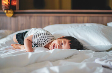 Portrait of Little boy wear striped shirt feel relax and laydown on the bed, looking at camera. A caucasian kid feel comfortable lying down on the bed with smiling face. Bed Vibes concept. Happy Kids.