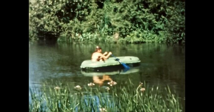 Young woman in boat on summer lake. Happy girl in bathing suit rows boat in green river nature. Natural holiday vacation at summer days. Vintage color film. Retro 80s, 90s archive. 1980s-1990s 