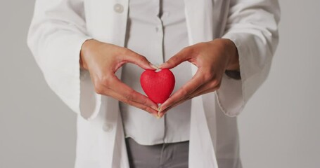 Video of biracial female doctor holding heart on white background - Powered by Adobe