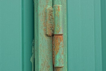 one iron green door hinge in rust on a metal gate on a wall in the street