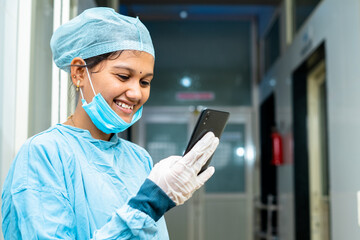 Happy smiling medical practitioner busy using mobile phone at hospital corridor - concept of using...