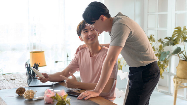 Young smiling gay couple working on new project and shooting pictures of new product by smartphone