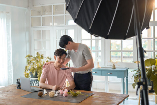 Young smiling gay couple working on new project and shooting pictures of new product by smartphone