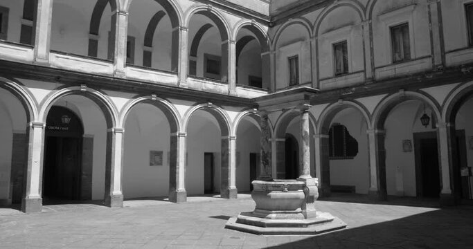 Naples, Italy. Black and white shot of a courtyard in Certosa di San Martino, a monumental charterhouse at daytime. Overview of the large cloister with numerable windows and doors.