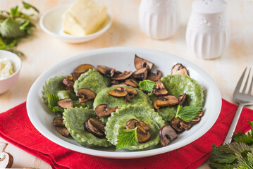 Round nettle ravioli stuffed with mushrooms and curd cheese in a gray ceramic plate on a light concrete background. Recipes with wild herbs.