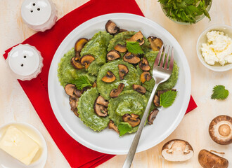 Round nettle ravioli stuffed with mushrooms and curd cheese in a gray ceramic plate on a light concrete background. Recipes with wild herbs.