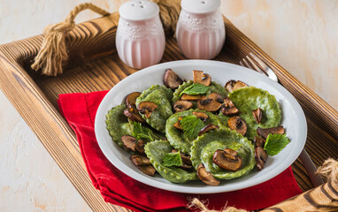 Round nettle ravioli stuffed with mushrooms and curd cheese in a gray ceramic plate on a light concrete background. Recipes with wild herbs.