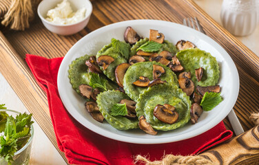 Round nettle ravioli stuffed with mushrooms and curd cheese in a gray ceramic plate on a light concrete background. Recipes with wild herbs.