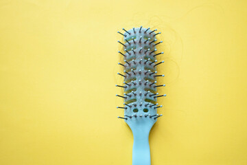 Fallen hair in a hairbrush. A green comb with fallen hair on a yellow background. Daily hair loss problem.