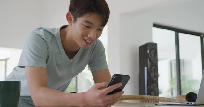 Asian male teenager using smartphone and smiling in living room