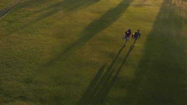 Two Diverse Male Golf Players Walking At Golf Course On Sunny Day