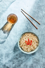 High angle view of served Asian food. Bowl with noodles decorated with slices of red chilli pepper on top and glass of drink. Chopsticks laying on plate