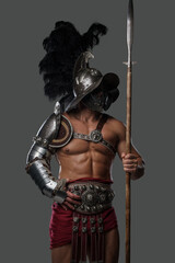 Portrait of antique roman gladiator dressed in helmet and light armor holding spear.