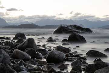 a large smooth stone in the water on the lake shore against the background of mountains is a long exposition.