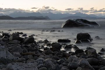 Obraz premium a large smooth stone in the water on the lake shore against the background of mountains is a long exposition.