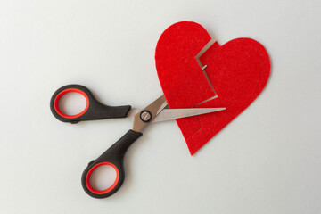 Scissors cut through the red decorative heart on a gray background. The theme of the heart as a...