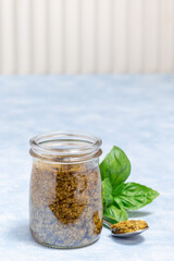 Basil green pesto sauce in glass jar and in spoon, on light blue background, vertical