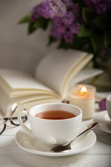 A cup of green tea against the background of a spring bouquet of lilacs on a textured gray background.Romantic composition with books and candles. Spring tea drink. Side view. Place to copy.
