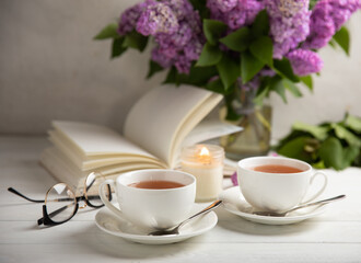 A cup of green tea against the background of a spring bouquet of lilacs on a textured gray background.Romantic composition with books and candles. Spring tea drink. Side view. Place to copy.