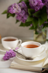 A cup of green tea against the background of a spring bouquet of lilacs on a textured gray background.Romantic composition with books and candles. Spring tea drink. Side view. Place to copy.