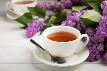 A cup of green tea against the background of a spring bouquet of lilacs on a textured gray background.Romantic composition with books and candles. Spring tea drink. Place to copy.